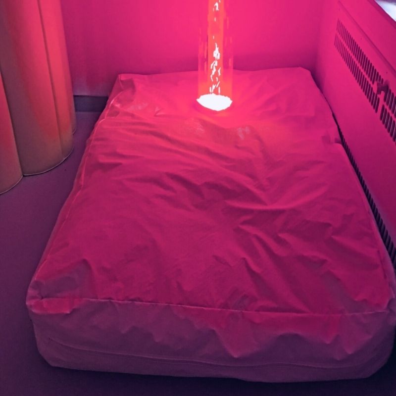 TFH Bubble Tube Cuddle Cushion in a sensory room with red LED bubble tube light, showing the large wipeable vinyl beanbag surround designed for 6-inch TFH bubble tubes