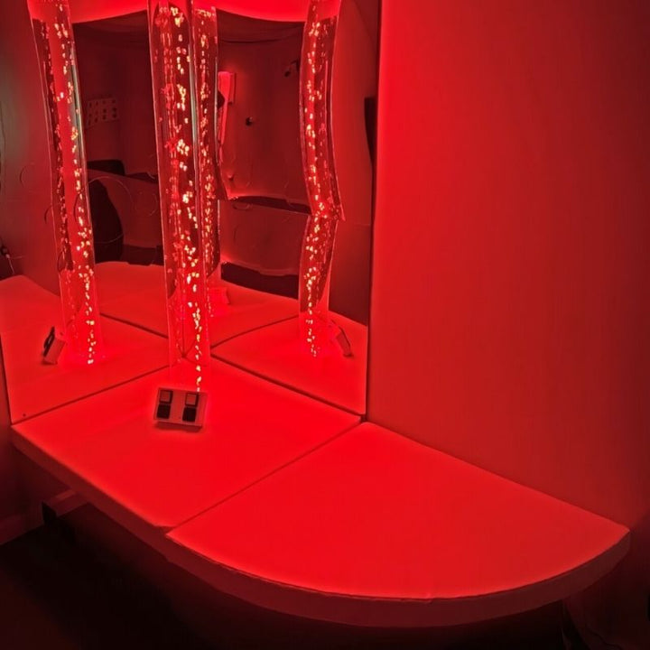 TFH Bubble Tube Corner Seat Base in sensory room with bubble tube glowing in red LED light, demonstrating mirrored base reflection