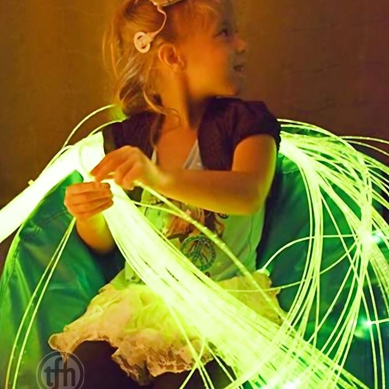 Child playing with TFH Fibre Optic Tails in green lighting, developing fine motor skills and visual tracking through sensory play