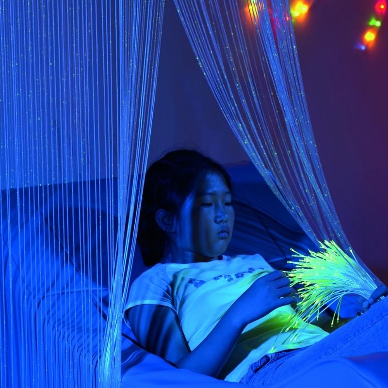 TFH Fibre Optic Waterfall with a child actively playing beneath 200 cascading fibre optic tails glowing in blue, showing the ceiling-suspended sensory light installation in a sensory room