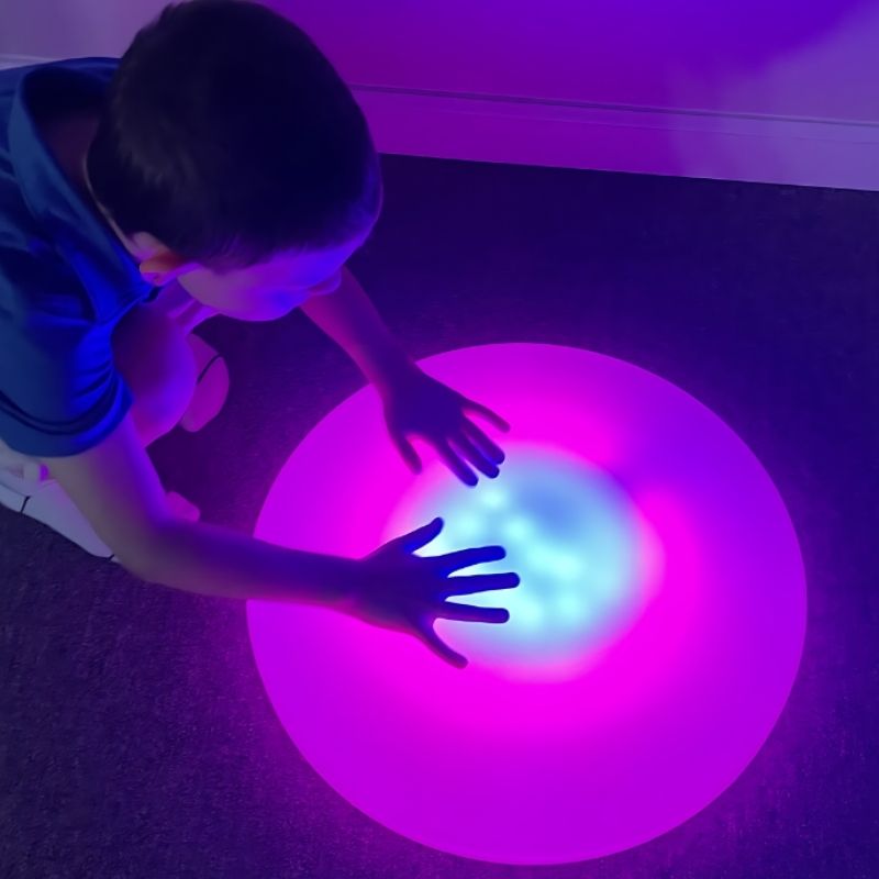 Child stepping on TFH Illuminated Floor Splot interactive sensory light tile, demonstrating cause-and-effect colour change