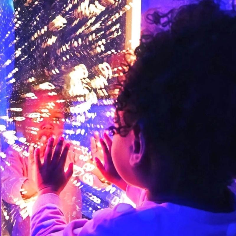 Child actively engaging with the TFH Genie Infinity Bubble Wall in a sensory room, showing the app-controlled LED colour display and infinite bubble reflection effect