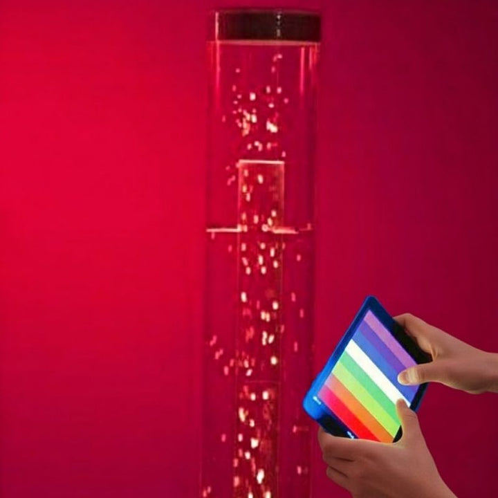 TFH Genie Whirlwind Tube and Base Kit Waterless 80-inch variant in red light with a user holding the MSE Genie App controller, showing the full-height Bluetooth waterless sensory column in use