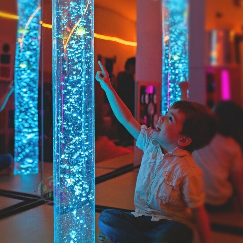 Child sitting and pointing at the TFH Giant Water Bubble Tube 8" Wide, demonstrating interactive engagement with the sensory bubble tube