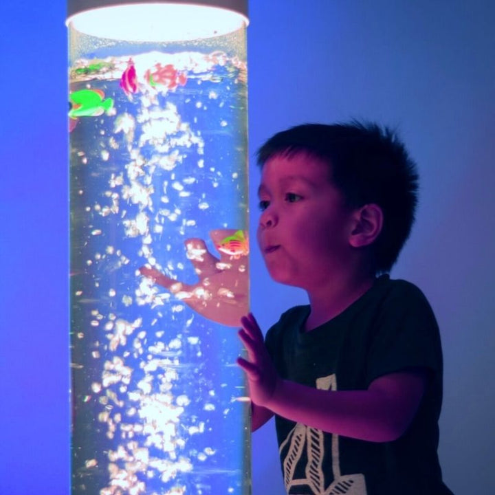 Boy gazing at the TFH Giant Water Bubble Tube 8" Wide in a sensory room, showing the large diameter column with colour-changing LED bubbles