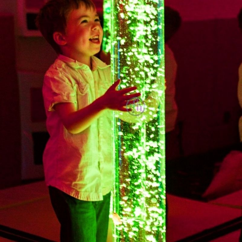 Boy smiling while touching the TFH Giant Water Bubble Tube 8" Wide acrylic surface, showing tactile sensory input from the wide diameter column