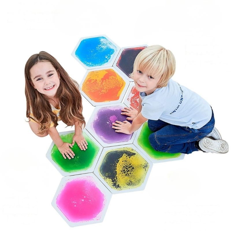 Two children actively playing on the TFH Hexagon Liquid Floor Tiles 9 Set, stepping and hopping to create colour-swirling liquid movement across the sensory floor tiles