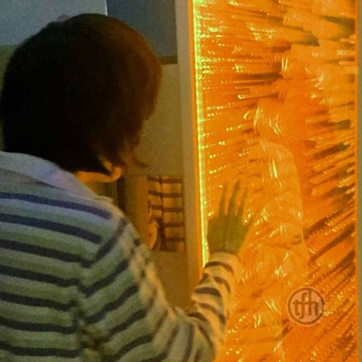 Back view of a child touching the TFH Infinity Bubble Wall lit in orange, showing tactile and visual sensory stimulation through direct wall contact