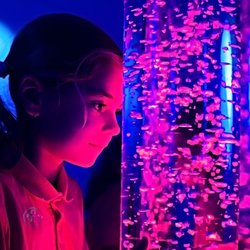 Girl leaning against the TFH Interactive LED Bubble Tube, engaging with the wired colour controller for sensory room play