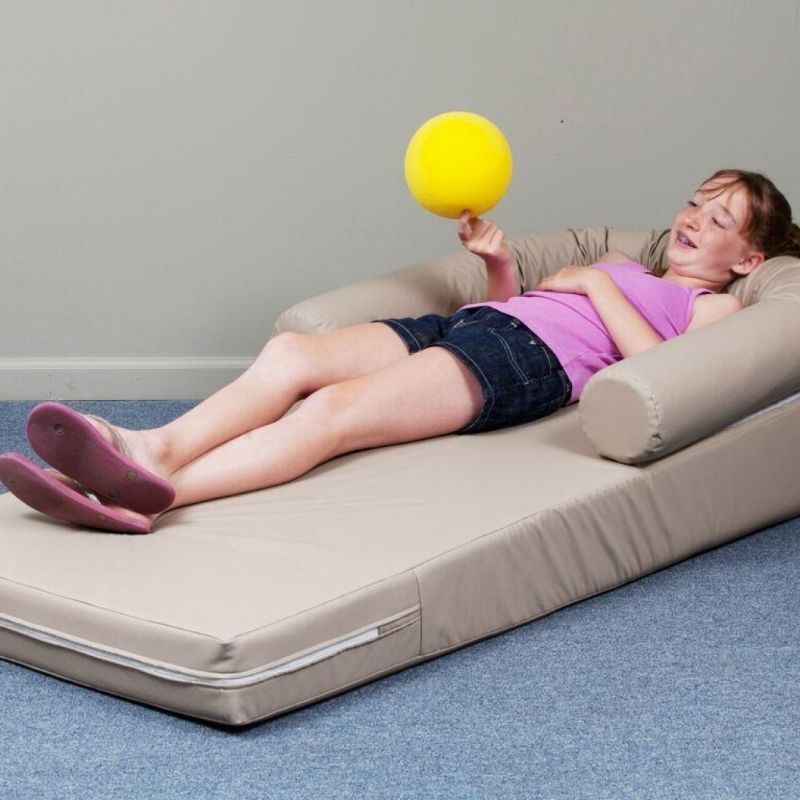 Child resting in the TFH Long Easy Comfort Lounger, showing the body-contouring foam sensory seating and curved head roll support for therapy rooms and sensory spaces