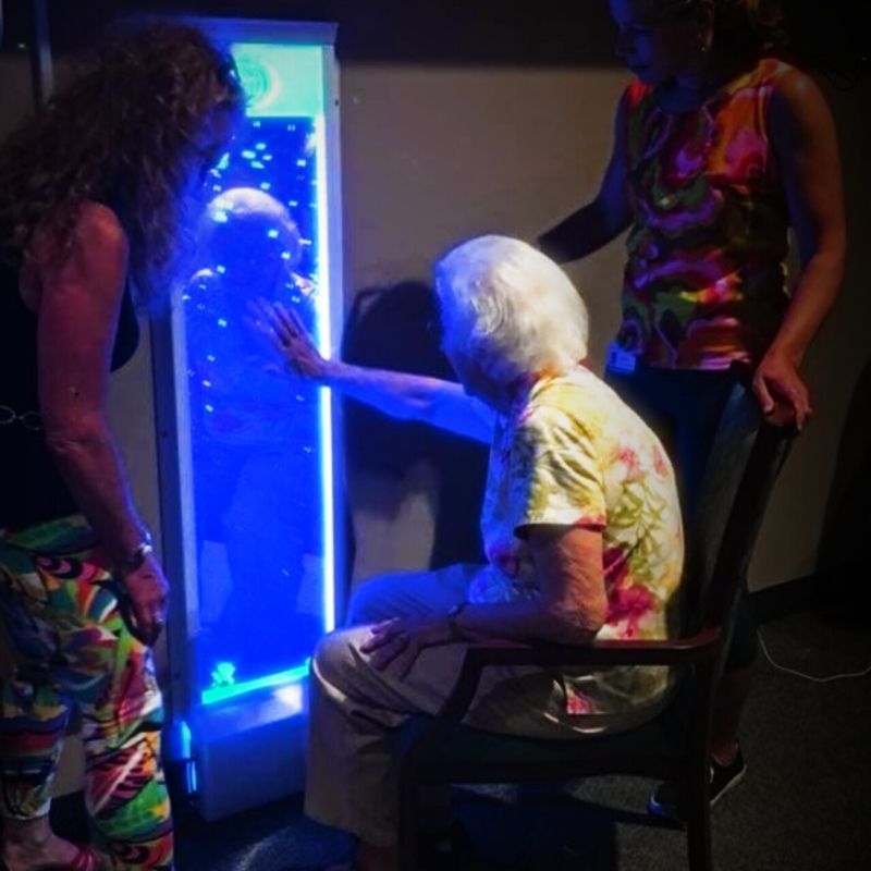 Older adult seated in a chair touching the TFH Colour Changing Mirrored Bubble Wall in a care setting, showing the wall-mounted infinity sensory bubble wall in use