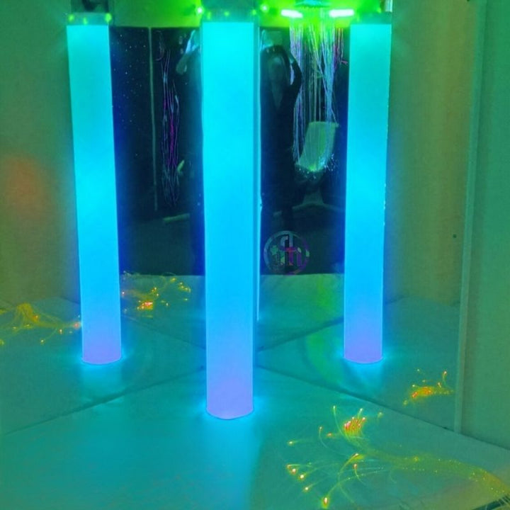 TFH Rainbow Frosted Tube in a room corner displaying blue-green rainbow colour cycling, showing the waterless sensory light column as a standalone visual therapy element in a multi-sensory space