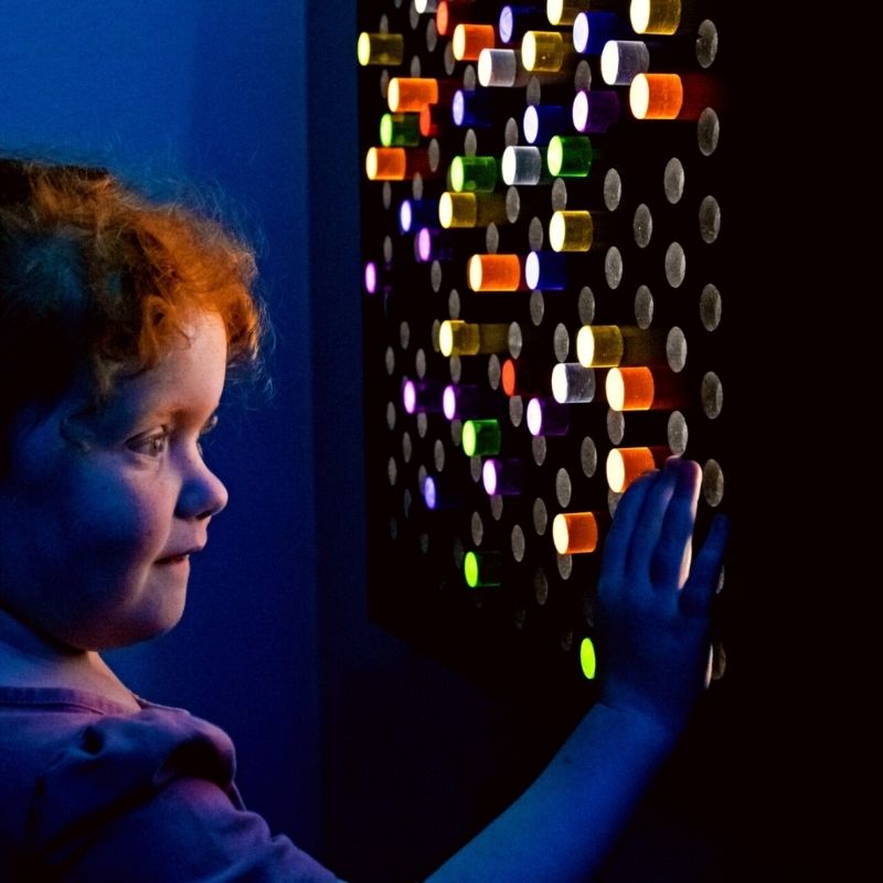 TFH Rod Wall Activity Panel with a child engaging from the side, showing the illuminated 144-rod panel in use as a fine motor and visual sensory therapy tool in a sensory room