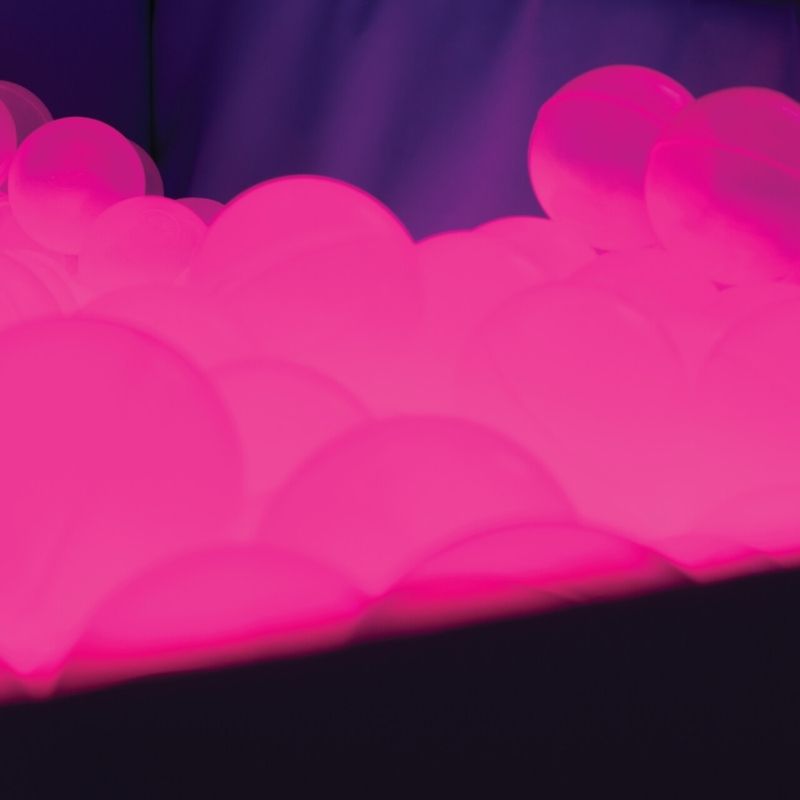 Close-up of TFH Light-Up Ball Pit translucent sensory balls glowing in pink LED light for visual sensory stimulation