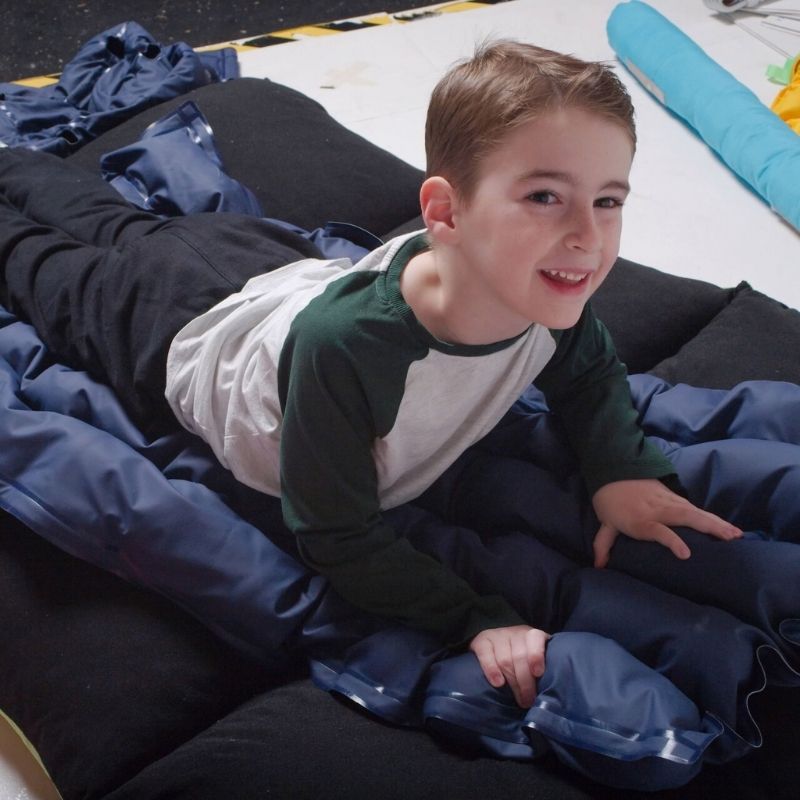 Child using the TFH Sensory Pressure Vinyl Ball Pad, experiencing dynamic deep pressure from large plastic balls for proprioception and body awareness