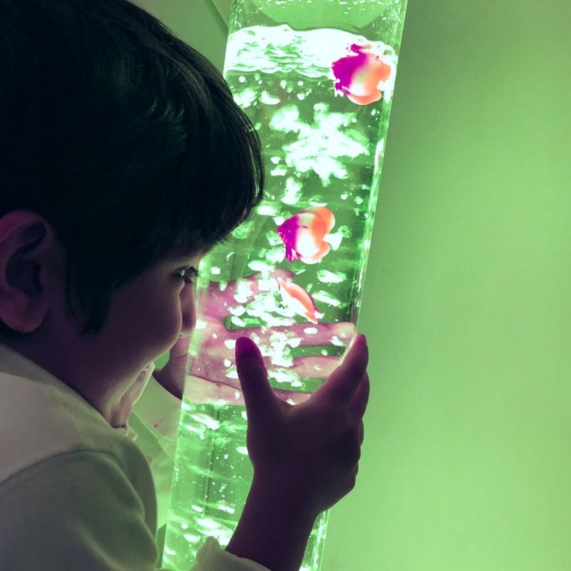 Child in active sensory play alongside TFH Small Bubble Tube 4" showing the compact colour-changing LED bubble column for bedroom and home sensory environments across North America