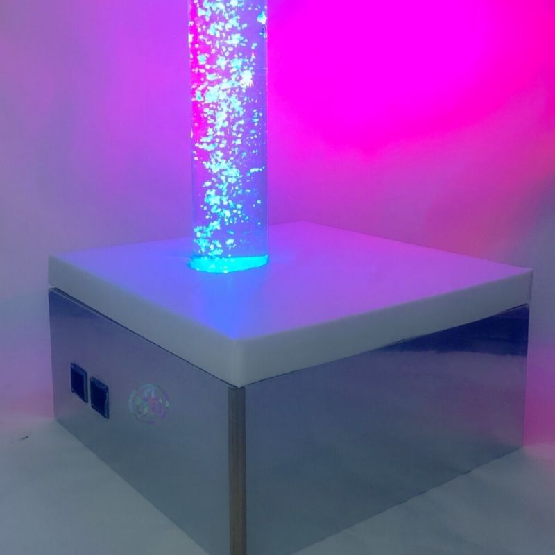 TFH Square Podium Base corner view with bubble tube glowing in pink light, demonstrating the mirrored sides of the sensory room podium reflecting colour for visual sensory stimulation
