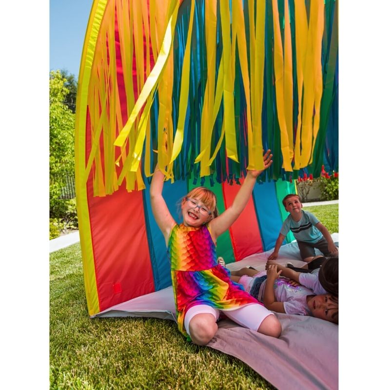Happy child walking through the TFH Giant Tickle Me Tunnel, experiencing full-body tactile sensory stimulation from the Velcro streamers