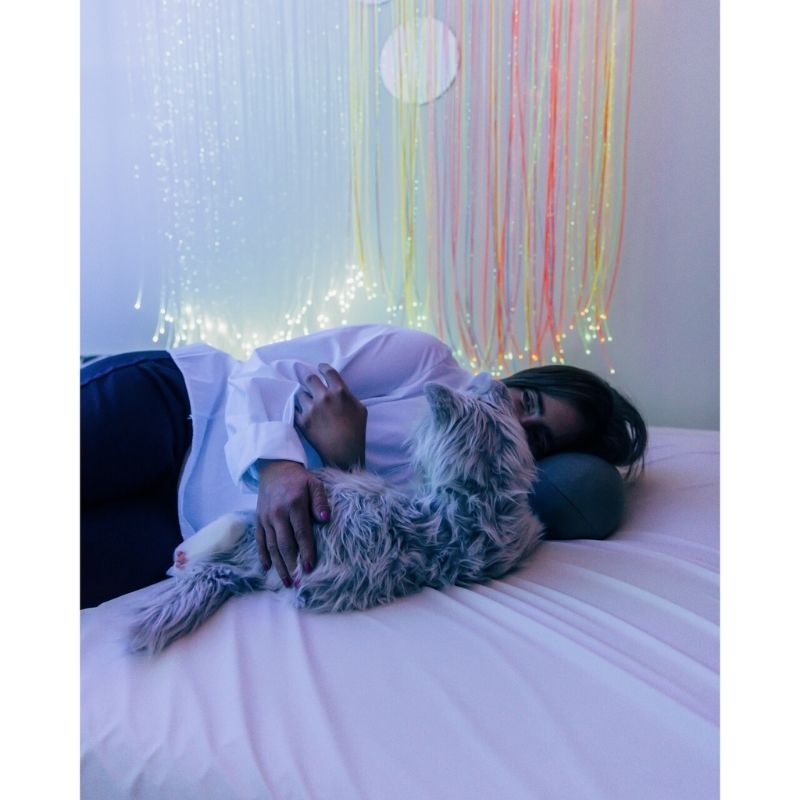 Person lying in bed with TFH UV Fibre Optic Tails glowing in a darkened room, showing use as a calming sensory light for bedrooms and quiet corners