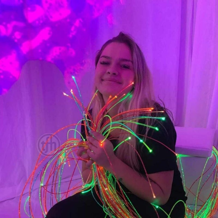 Woman holding TFH UV Fibre Optic Tails with Light Source, demonstrating safe tactile handling of glowing UV-reactive strands for sensory exploration