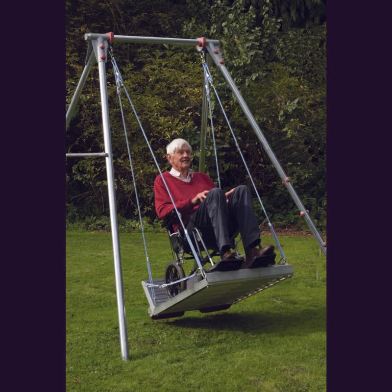 An older adult using his wheelchair on the TFH Wheelchair Platform Swing and frame, showing accessible vestibular play for users of all ages