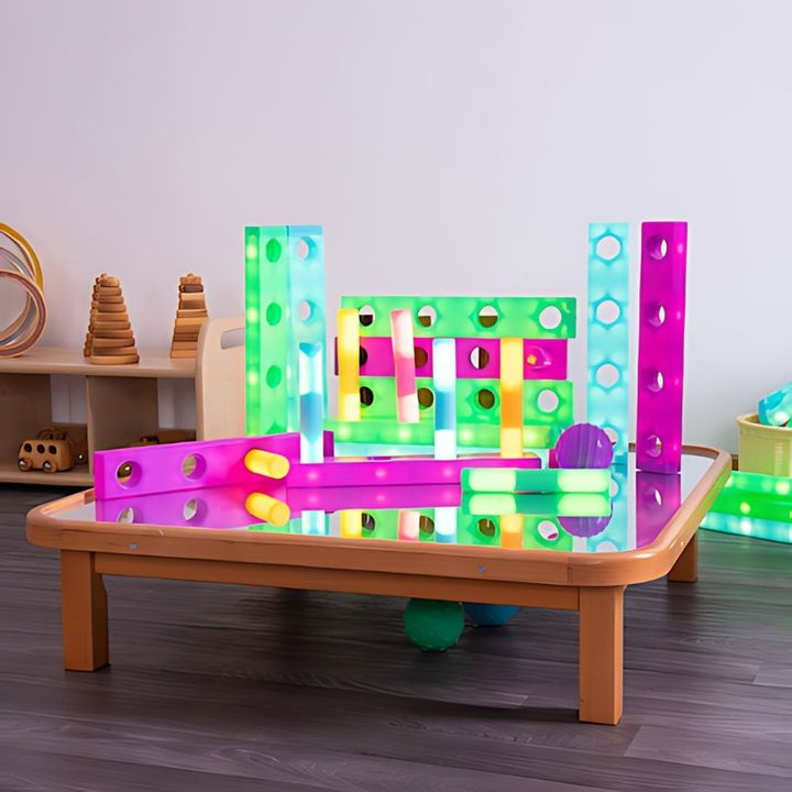 TTS Stack and Build Glow Blocks arranged as an illuminated construction on a light table in an early years classroom, demonstrating use in STEAM learning, sensory room building, and imaginative play