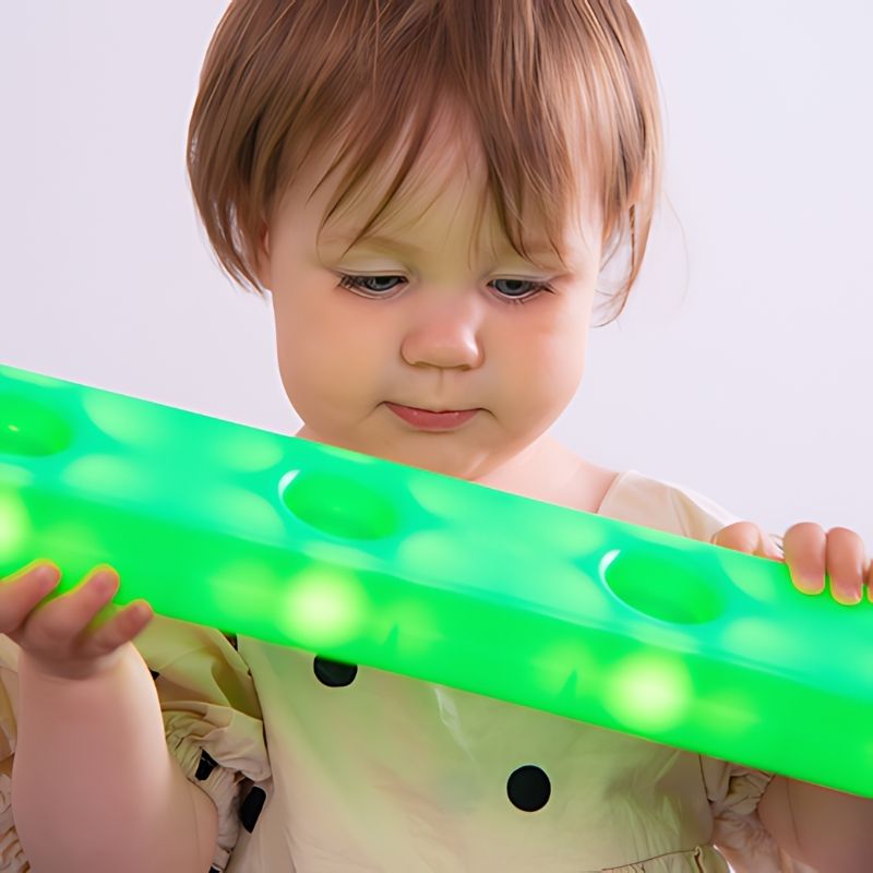 Toddler holding a single green TTS Stack and Build Glow Block and exploring its light and texture, highlighting tactile sensory engagement and cause-and-effect play for early learners