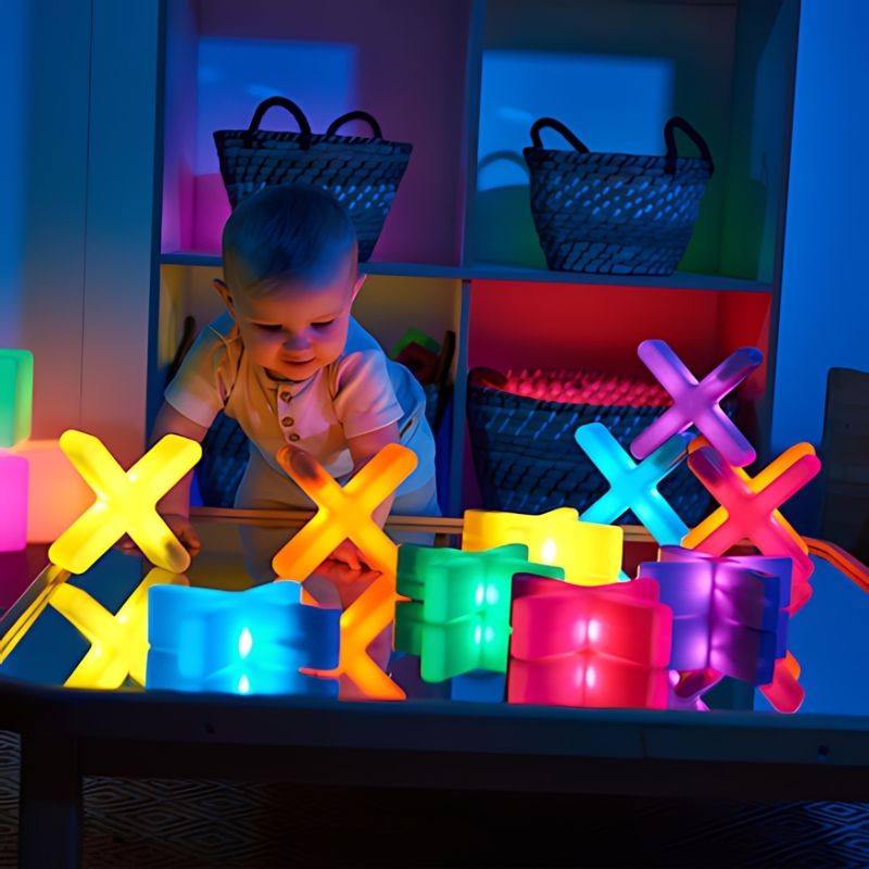 Baby reaching towards TTS Glow Crosses and light-up sensory construction blocks on a table in a darkened early years sensory room, supporting cause and effect discovery from infancy