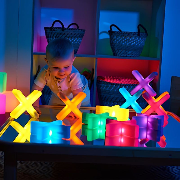 Baby reaching towards TTS Glow Crosses and light-up sensory construction blocks on a table in a darkened early years sensory room, supporting cause and effect discovery from infancy