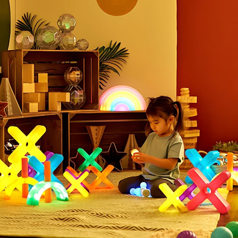Young child engaged in open-ended play surrounded by TTS Glow Crosses and complementary illuminated sensory resources in a warm home play space, demonstrating imaginative and sensory exploration