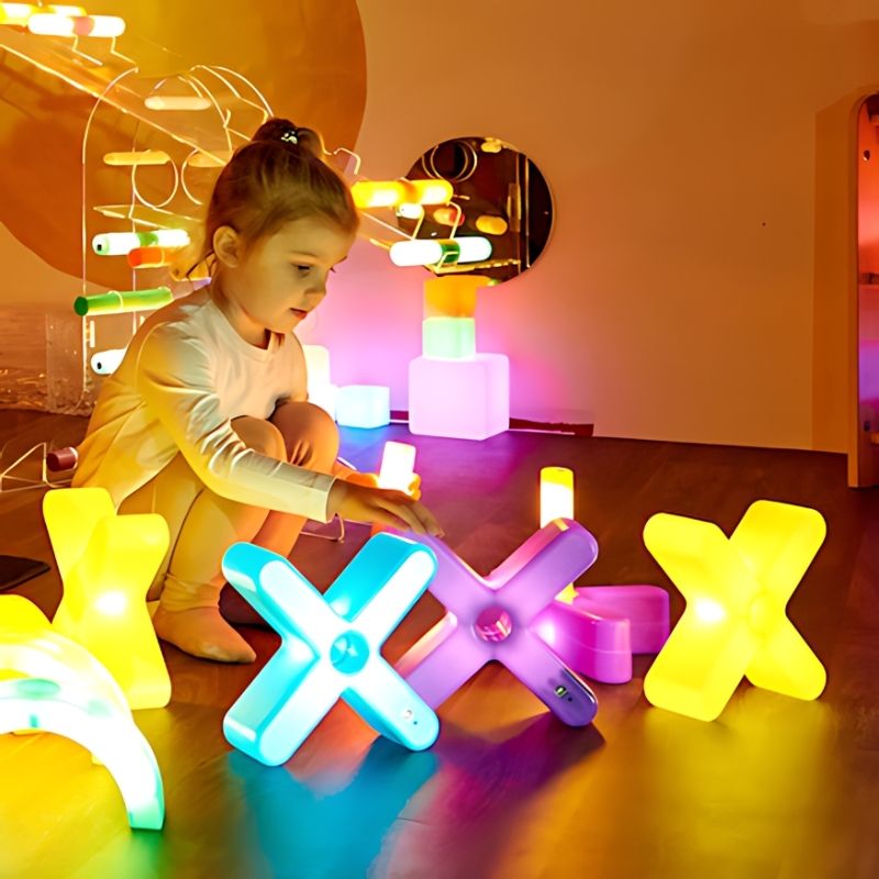 Young child playing with large TTS Glow Crosses in a warmly lit sensory room, exploring light up sensory construction toys in an early years setting