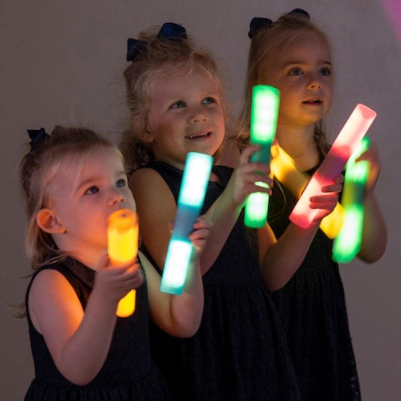 Three children holding TTS rechargeable glow cylinders, showing collaborative sensory light play and social learning in an early years setting