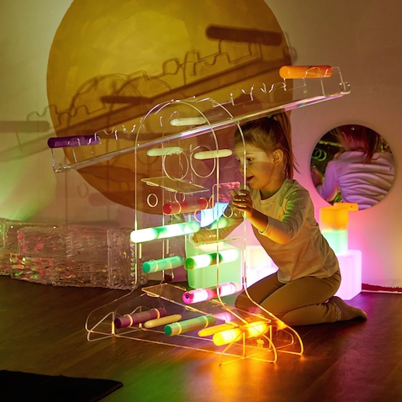 Child engaged in open-ended sensory light play with TTS Light Up Glow Cylinders on the floor, supporting fine motor development