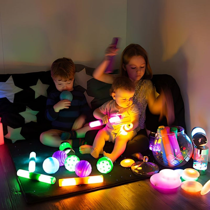 Three children engaged in collaborative light-up sensory play with the TTS Sensory Light Up Glow Collection, exploring glow cubes and rollers together