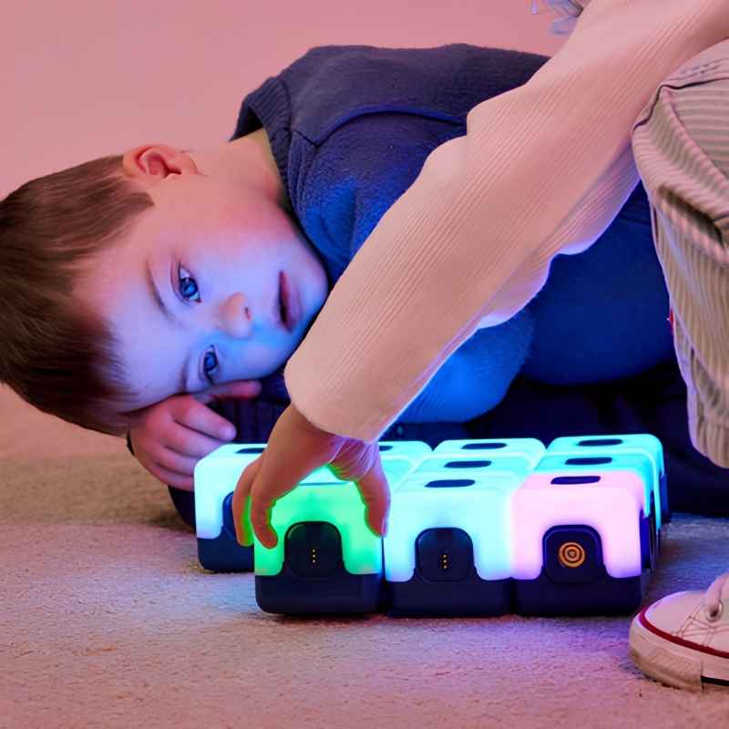 Young boy at floor level engaging with a row of magnetically connected TTS Glow Sequencing Cubes, demonstrating cause-and-effect sensory light play