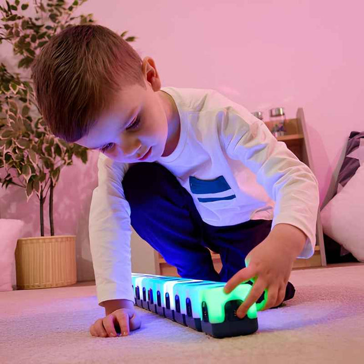 Young boy reaching to tap the end of a long magnetic row of TTS Glow Sequencing Cubes glowing in blue and green, demonstrating sequential sensory exploration