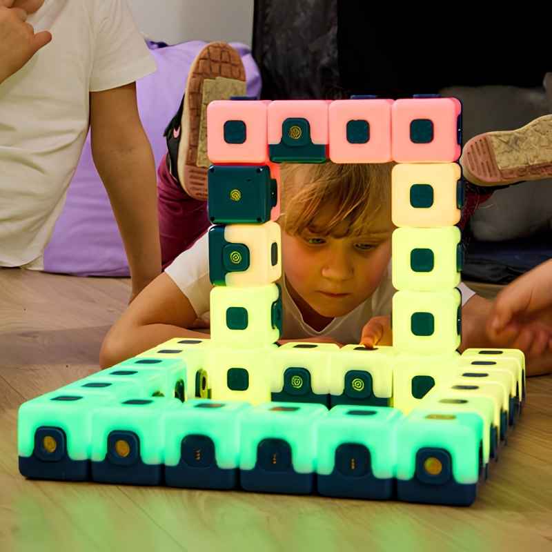 Two children collaboratively building a large illuminated arch structure with TTS Glow Sequencing Cubes in yellow-green and pink, showing open-ended construction and early maths play