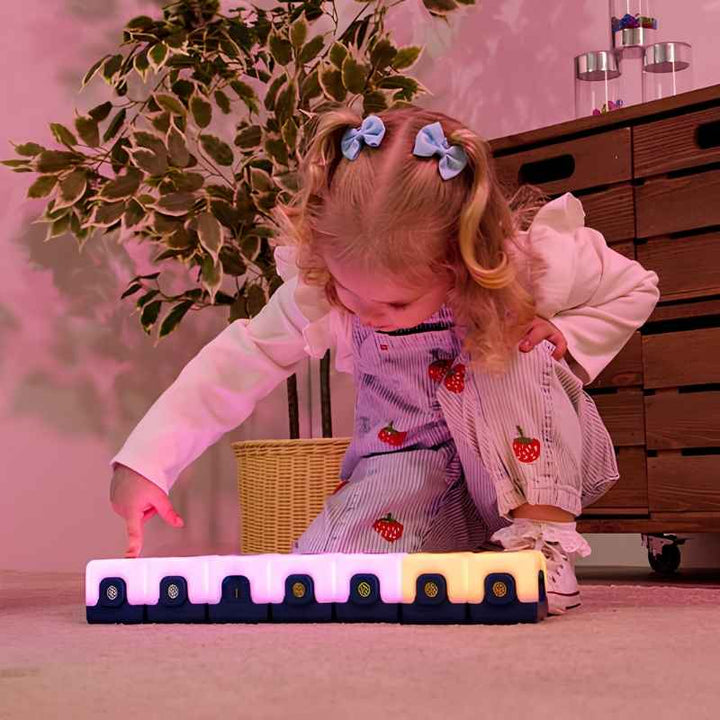 Young child tapping a connected row of TTS Glow Sequencing Cubes on the floor, exploring cause-and-effect colour change through sensory light-up play
