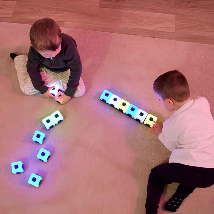 Two young children engaged in parallel play with TTS Glow Sequencing Cubes on a carpeted floor, each exploring colour and connection independently in a home or nursery setting