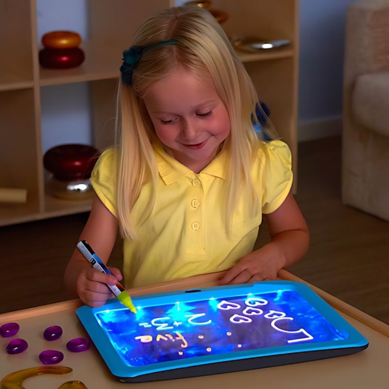 Girl using a TTS illuminated writing board from the Sensory ICT Glow Set for early years mark-making in a sensory room setting