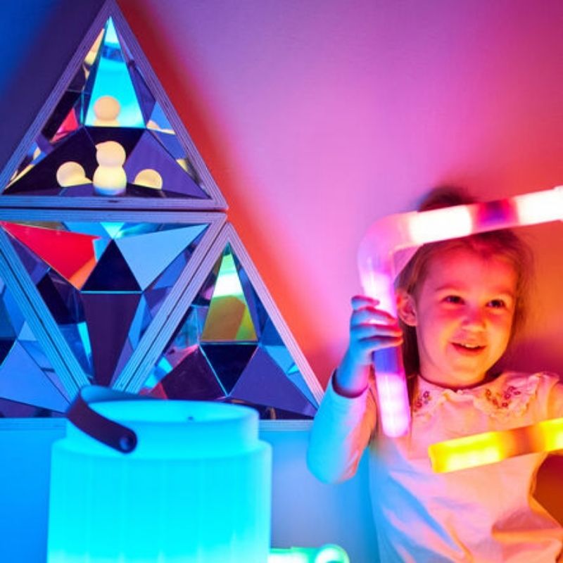 Child exploring reflections in the TTS Kaleidoscope Mirror with blue and red light hues, supporting visual sensory development