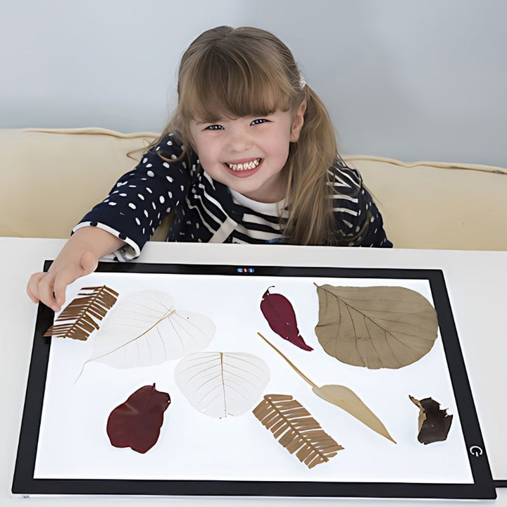 Child using the TTS Ultra-Bright LED Light Panel for nature-based sensory investigation with leaves, supporting visual learning and scientific inquiry
