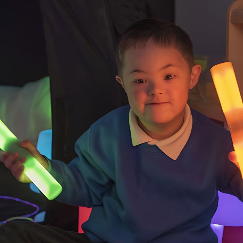 Boy holding two TTS glow cylinders in different colours, exploring visual sensory stimulation and colour recognition through active play