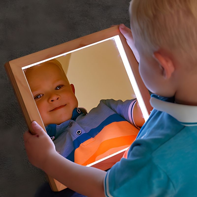 Young child holding TTS light up hand held mirror, demonstrating versatile sensory play with LED illuminated acrylic mirror for home and classroom use