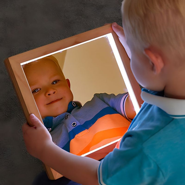 Young child holding TTS light up hand held mirror, demonstrating versatile sensory play with LED illuminated acrylic mirror for home and classroom use