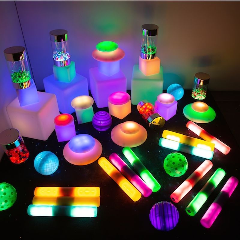 Complete TTS Sensory Light Up Glow Collection laid out in landscape, showing all five LED glow sets including cubes, pebbles, rollers, spheres, and cylinders