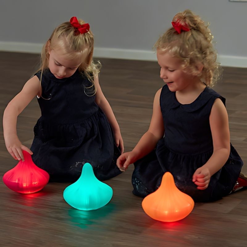 Two young children playing together on the floor with TTS Light Up Spinning Tops glowing red, teal, and orange, supporting shared sensory exploration and early years social play