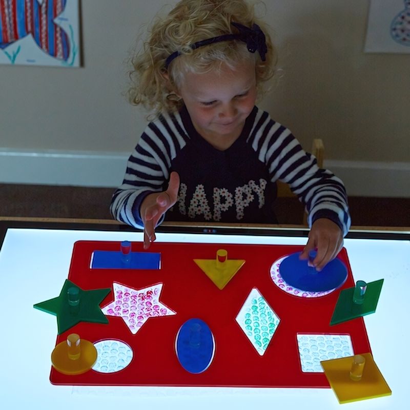 TTS Lightbox Acrylic Shape Sorting Board with eight geometric shapes illuminated on a light panel, a sensory fine motor toy for classrooms and therapy rooms