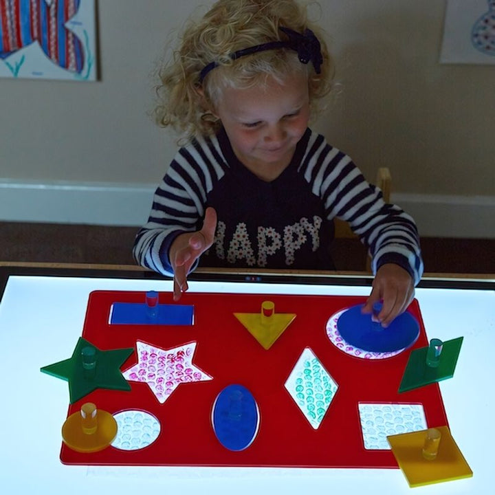 TTS Lightbox Acrylic Shape Sorting Board with eight geometric shapes illuminated on a light panel, a sensory fine motor toy for classrooms and therapy rooms