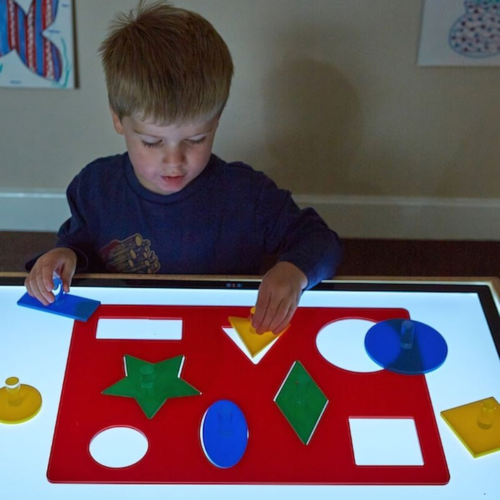 Child placing an acrylic shape into the TTS Lightbox Shape Sorting Board on a light panel, developing hand-eye coordination and shape recognition skills